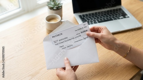 Person pulling a salary paycheck from an envelope near a laptop.