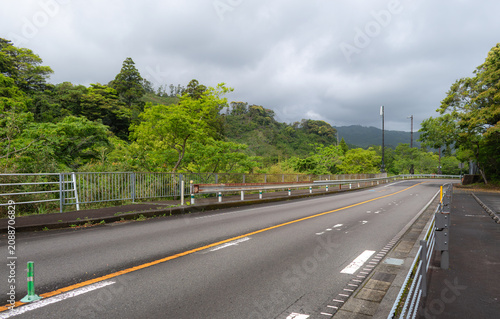 Bild auf Leinwand MIYAZAKI, JAPAN: An empty winding asphalt mountain road surrounded by lush green forests and rolling hills under a cloudy sky near Horikiri Pass (Horikiri-toge) along the Nichinan Coast in Kyushu