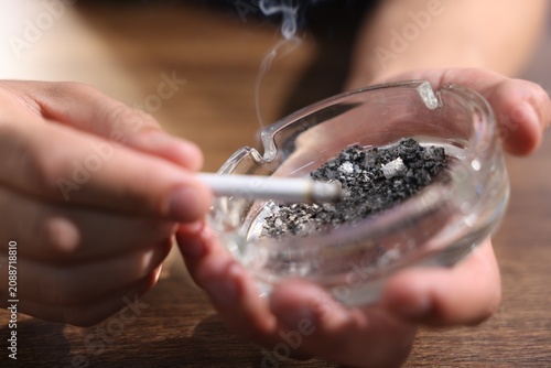 Картината върху платно Man flicking ash from cigarette into ashtray at wooden table, closeup