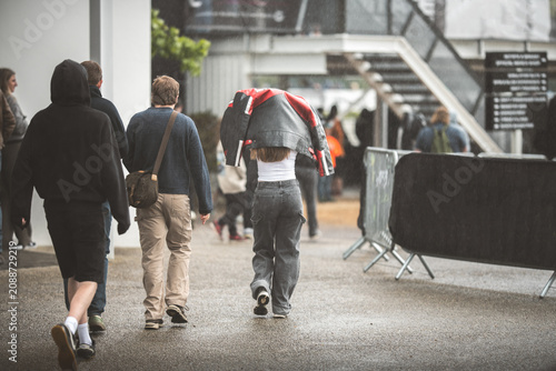 Tableau sur toile People walking in the rain, one person uses a jacket as an umbrella