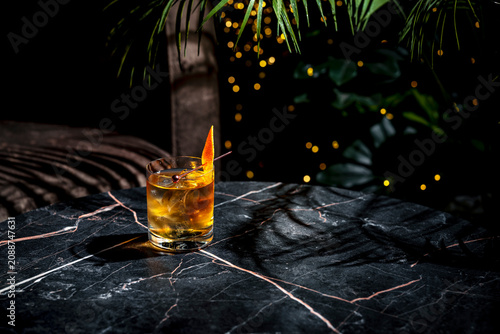 Fotografie Rusty nail scotch cocktail on wide marble bar table with shadows