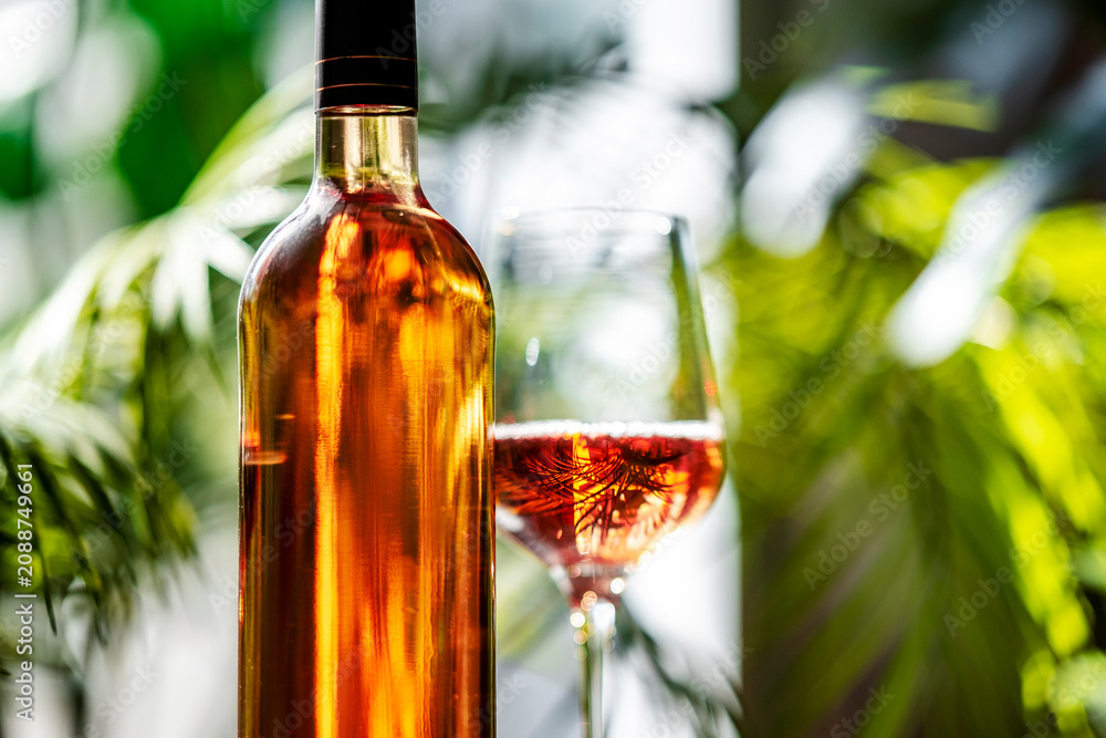 Obraz premium Rose wine bottle close up with glass on background. Tropical resort lounge terrace card and premium alcohol brand design concept.