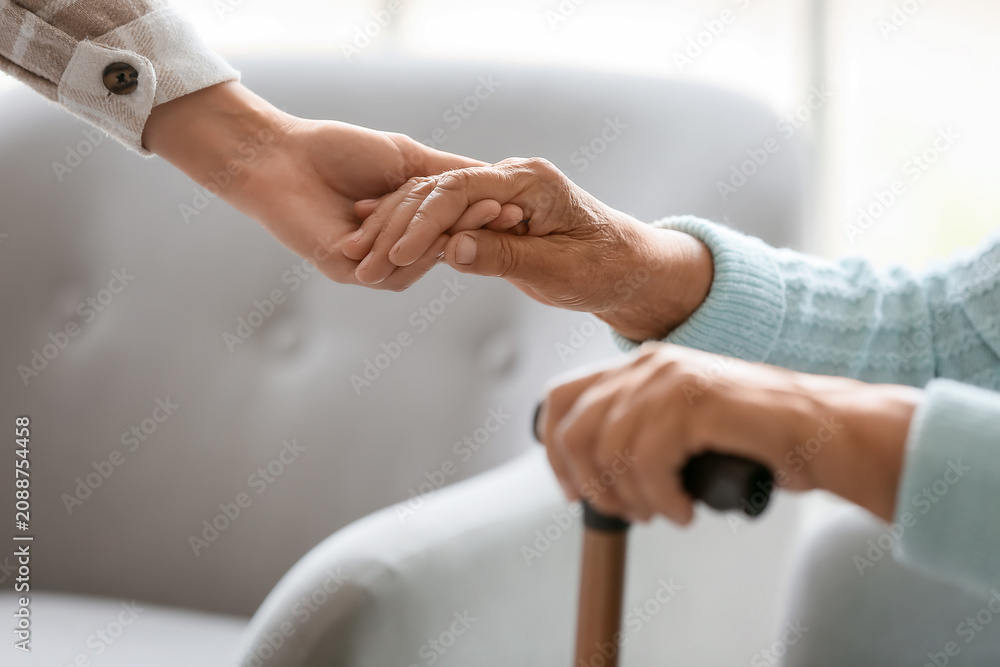 Fototapeta premium Senior woman with stick and daughter holding hands at home, closeup