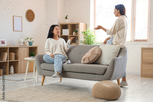 Beautiful young happy Asian sisters speaking on sofa at home
