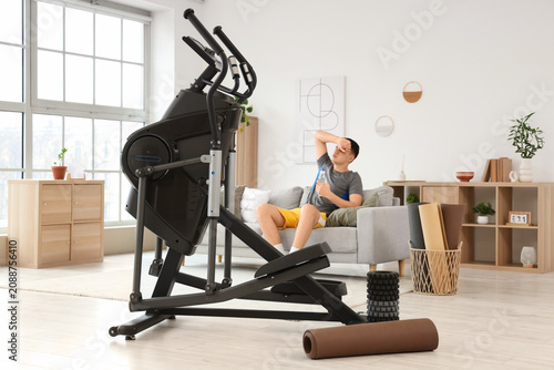 Tired young man resting after training on modern exercising bike at home