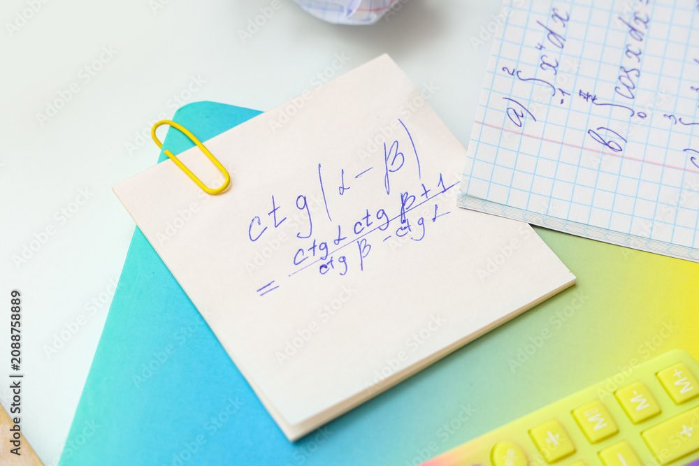 Obraz premium Sticky note with math formulas and notebook on light background, closeup