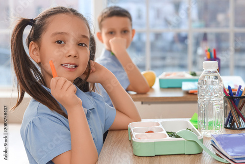 Cute little Asian schoolgirl having lunch in classroom, closeup