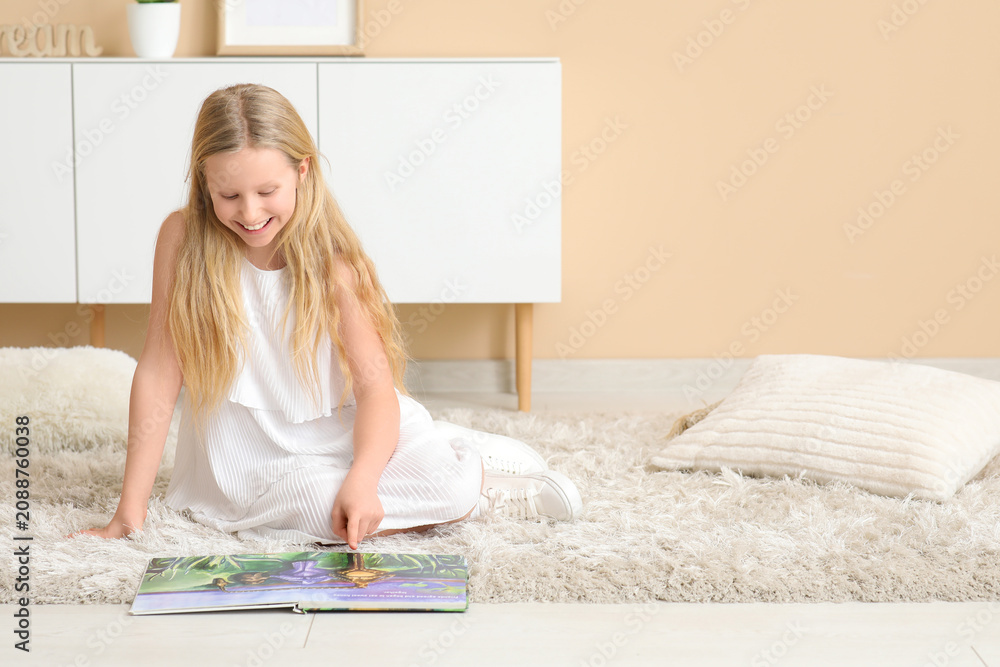 Obraz premium Little girl reading book while sitting on floor at home