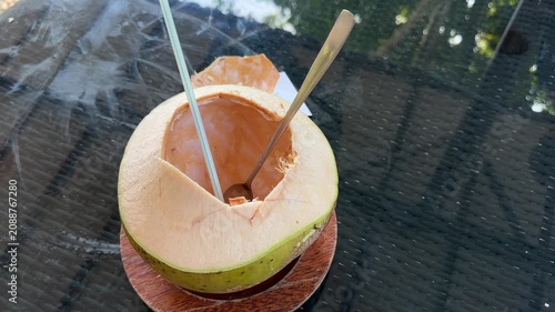 Opening Fresh Coconut with Straw and Spoon on Glass Table