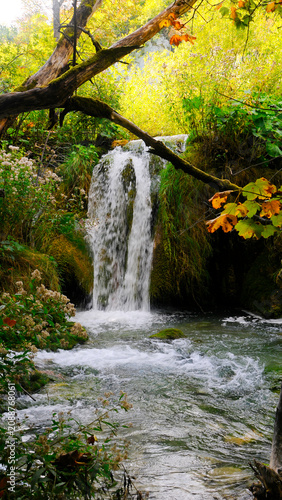 Forest waterfall spilling into pond surrounded by brilliant Autumn foliage