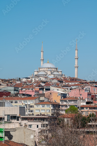 vertical photo of a cityscape view of a ottoman mosque in a hill surrounded by buildings with a clear sky.
