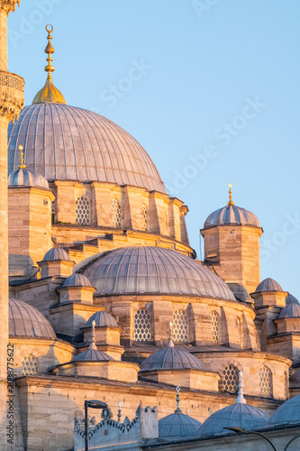 Vertical photo of an ottoman mosque facade with ther domes and minaret.