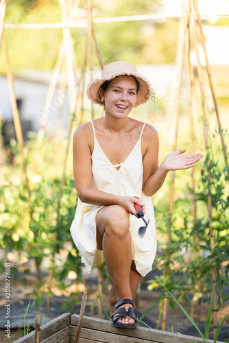 Photos Rural dweller girl in straw hat with garden tools watering can against backgroun