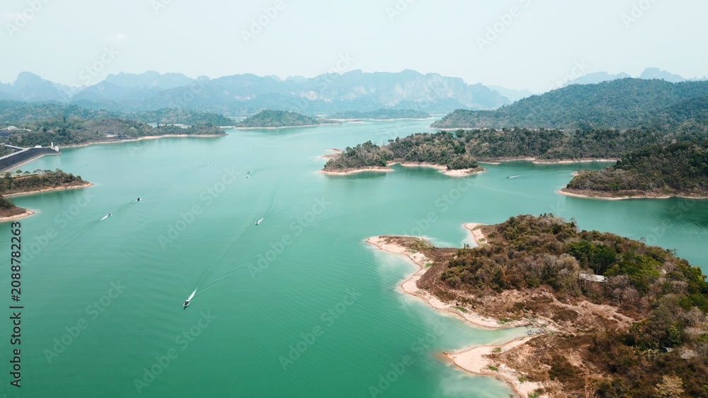 Naklejka premium Khao sok lake water reservoir with longtail boats navigating between limestone islands