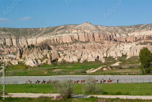 Side view of a row of Horse riders riding past ancient fairy chimney rock formations, Cappadocia, Anatolia, Turkey