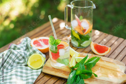 Close-up of a glass of water, mint leaves and assorted citrus fruit on a garden with a pitcher and napkin on a table in summer