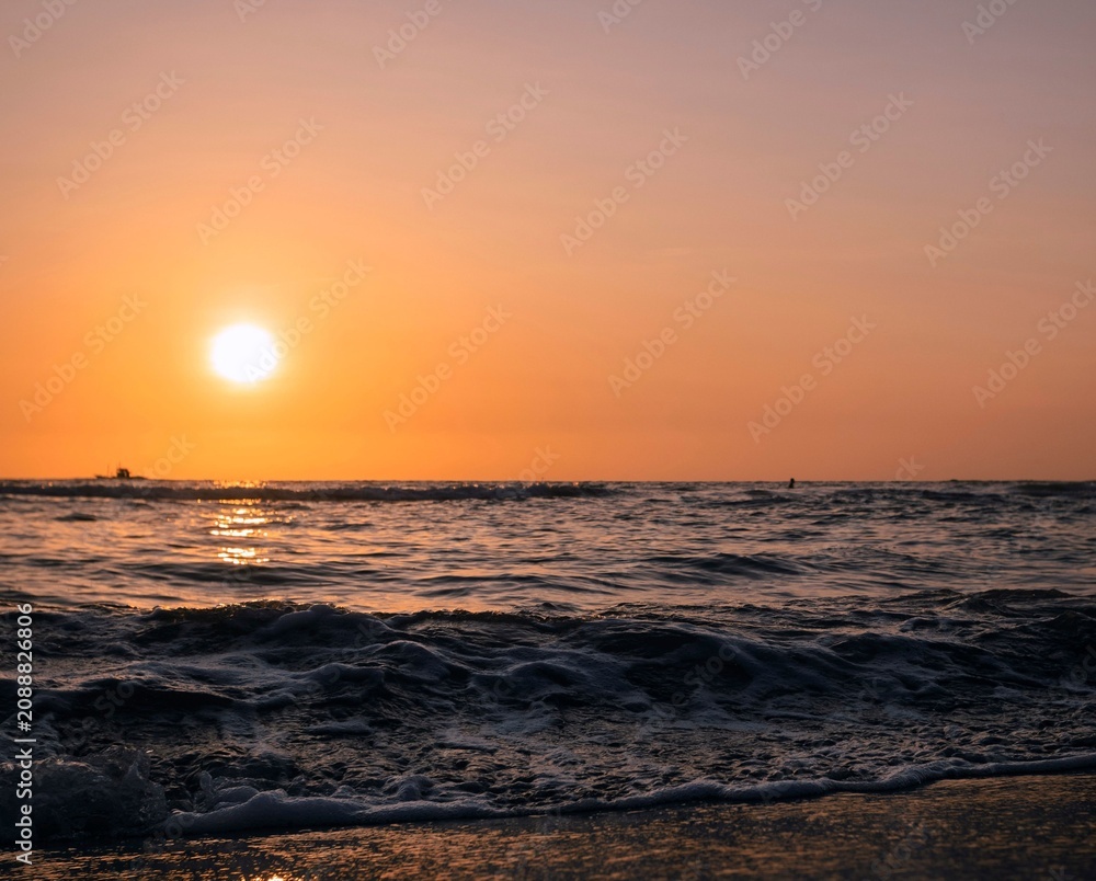 Obraz premium Peaceful beach at sunset featuring gentle ocean waves, golden light, and a colorful evening sky.