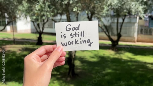 Hand with christian faith motivational concept - God is still working, on the nature background