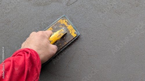 Foto Hand worker applying fresh wet cement mortar with steel trowel on concrete wall