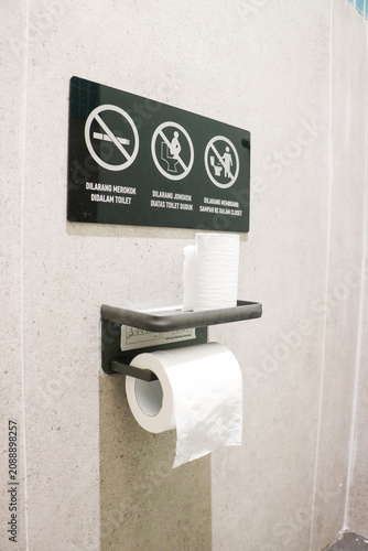 Vászonkép A black public restroom sign with explicit rules mounted above a metal toilet pa