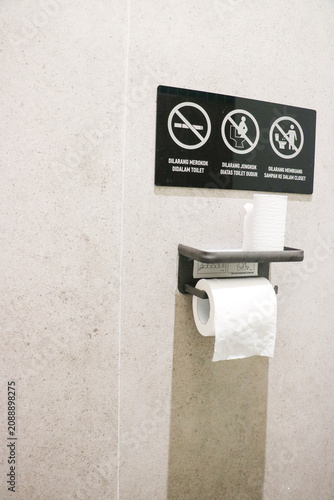 Foto A black public restroom sign with explicit rules mounted above a metal toilet pa