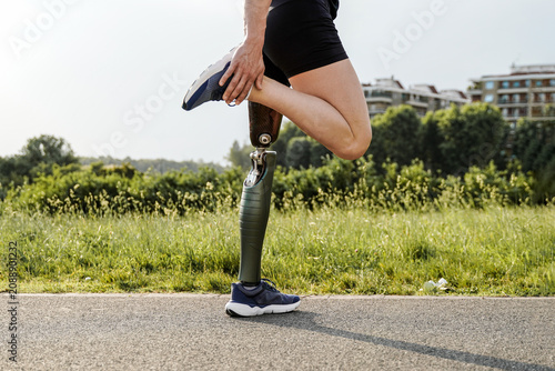Athletic man with disability doing sports at park city - man with prosthetic leg stretching before exercise routine - Physical disability, healthy lifestyle concept