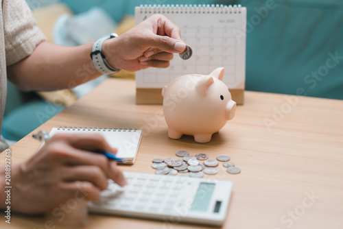 Accountant hand pressing calculator and inserting coin into pink piggy bank. Business person managing salary income, household expense, finance budget and tax