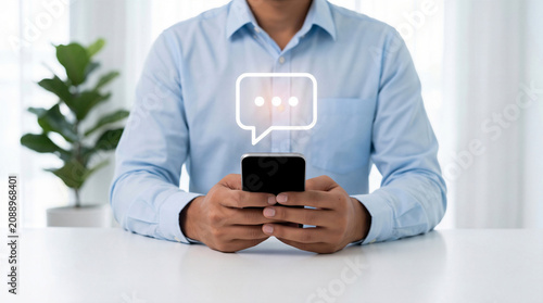 Businessman using smartphone with digital chat bubble icon representing AI chatbot, online messaging, and virtual customer support
