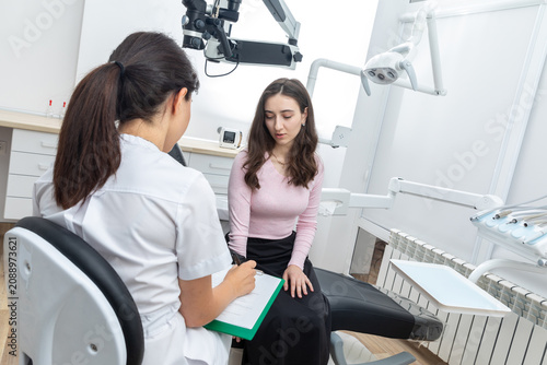 фотографія Female dentist filling in papers while talking to young patient in dental office