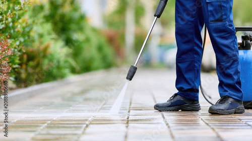 Pressure washing, Exterior cleaning. Worker cleans a paved walkway with a high pressure washer, removing dirt and restoring outdoor surfaces for property maintenance.
