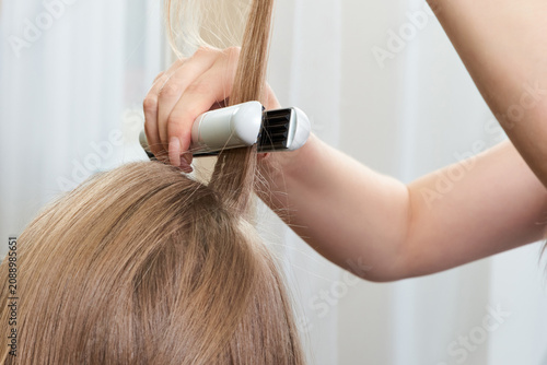 фотографія Hairstylist working on woman client with crimper