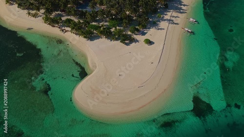 Aerial drone flight flying backwards to reveal Tangkahan Island, Balabac, Palawan, Philippines. Reverse tracking pull-away shot showcases tropical white sandbar, palm trees, and turquoise reef.