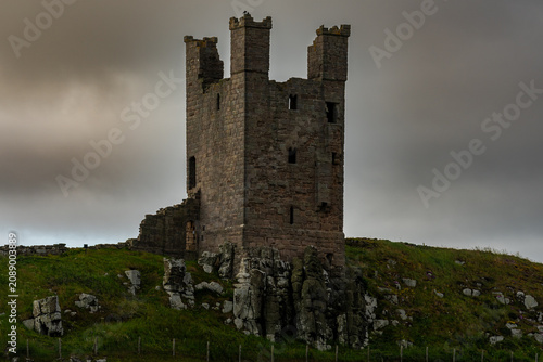 Dunstanburgh Castle keep ruins standing on grassy headland under stormy sky