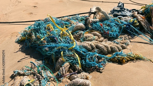 Schilderij op canvas Tangled discarded blue fishing nets and ropes washed ashore on a sandy beach, symbolizing marine plastic pollution