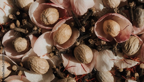 Flat lay of peony petals scattered over whole nutmeg dried cloves and saffron threads filling entire frame warm pastel and amber tones