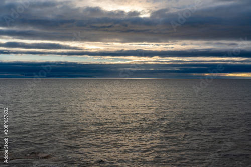 Layered stratus clouds glowing above open sea with light breaking through horizon band