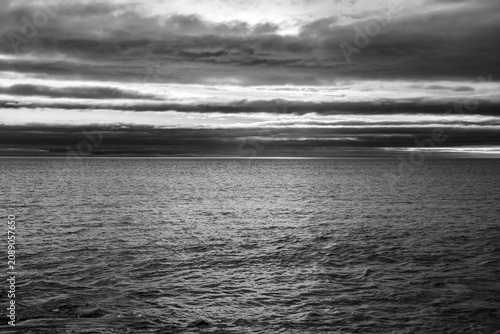Layered storm clouds hanging over textured open sea in black and white
