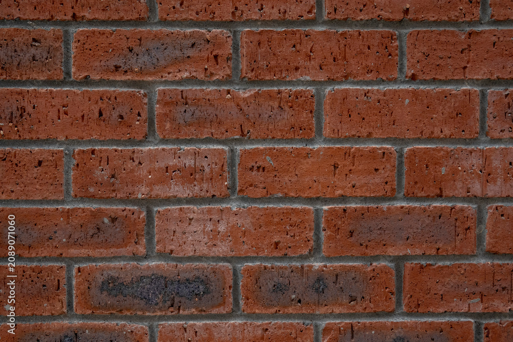 Fototapeta premium Weathered red brick wall texture with rich terracotta and crimson tones. A rigid masonry grid featuring a rough matte finish and dark charcoal accents for versatile industrial design utility.