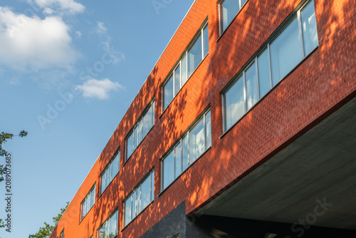 Contemporary university building with red brick facade, blue sky and tree shadows