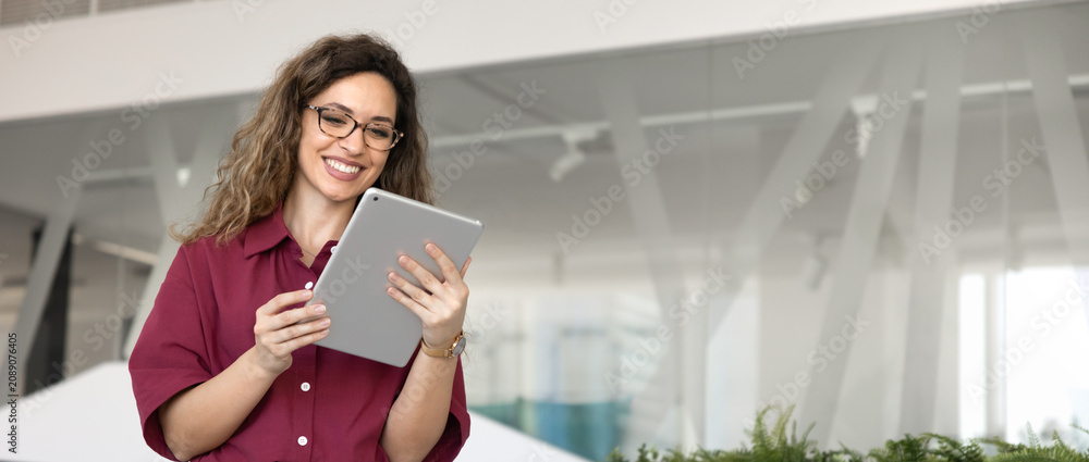 Fototapeta premium Smiling businesswoman browsing information, engaged in corporate or business communication via digital tablet in corporate office, copyspace banner. Technology, professional application use concept