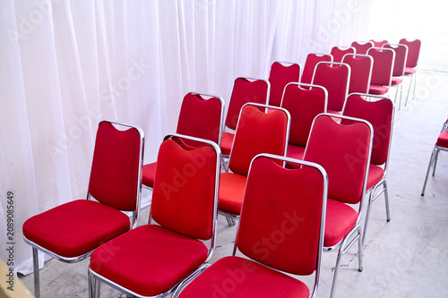 Rows of neat red banquet chairs with chrome legs arranged for an event or seminar, set against a soft white draped curtain background.