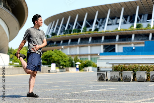 Foto 屋外で太ももや股関節を伸ばし柔軟性や可動域を高めケガ予防を行うスポーツウェアを着た男性のスポーツマン