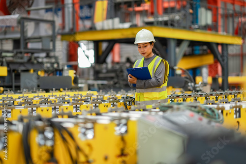 Foto Female industrial engineer inspecting manufacturing equipment and recording production information on clipboard