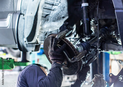 Professional mechanic replacing car brake disc and suspension components in a garage workshop.
