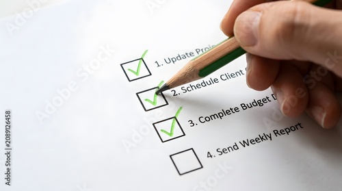 Hand checking off completed tasks on a to do list with a green pencil representing productivity and achievement