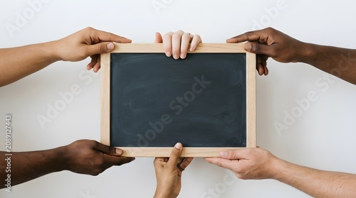 Diverse hands collaboratively holding a blank wooden framed chalkboard against a plain white backdrop symbolizing unity
