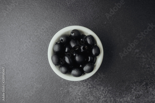 Canvastavla Top view of white bowl filled with black olives on stone background