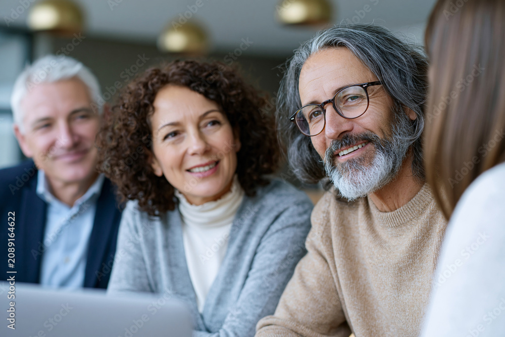 Fototapeta premium Three smiling adults gather around a laptop. Their expressions convey warmth and engagement. The scene suggests collaborative learning or group discussion