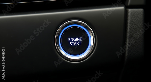 Close-up of a modern cars engine start button with a blue glowing ring on a black dashboard