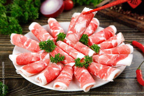 Gourmet Raw Meat Slices with Marbling on Plate Ready for Cooking with Fresh Herbs and Vegetables